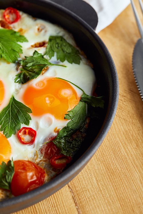 close up view of fried eggs with parsley and chili pepper on wooden table