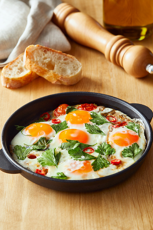 fried eggs with parsley and chili pepper on wooden table with bread