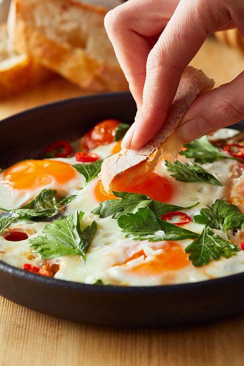 cropped view of eating fried eggs with bread at wooden table