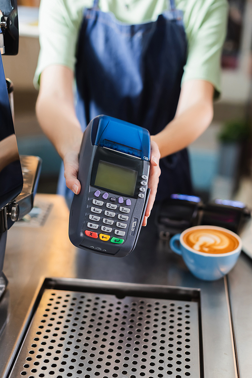 Cropped view of blurred barista holding payment terminal near coffee in cafe