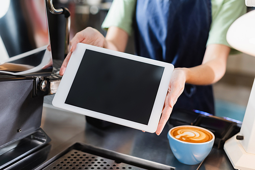 Cropped view of barista holding digital tablet with blank screen near coffee in cafe
