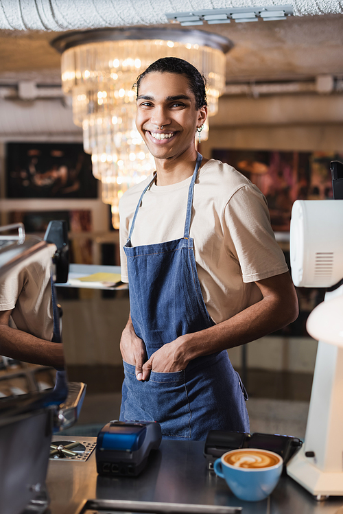 Smiling african american barista  near payment terminals and coffee in cafe
