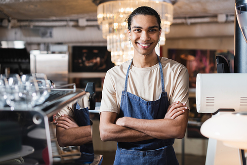 Smiling african american barista crossing arms in cafe