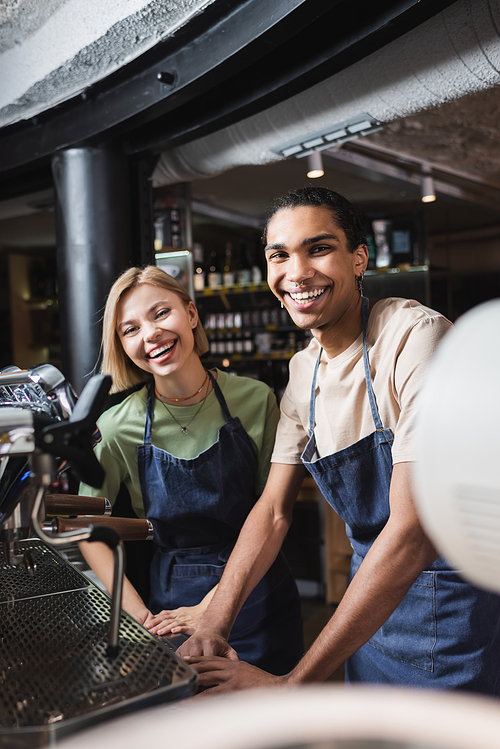 Cheerful interracial baristas  near coffee machine in cafe