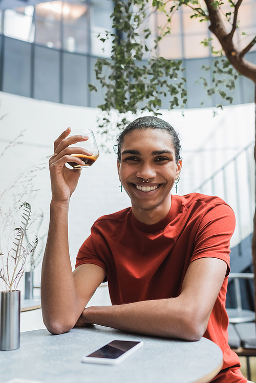 Smiling african american man holding coffee near cellphone in cafe