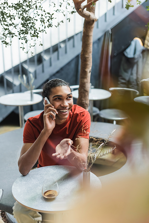 Positive african american man talking on cellphone near coffee in glass in cafe