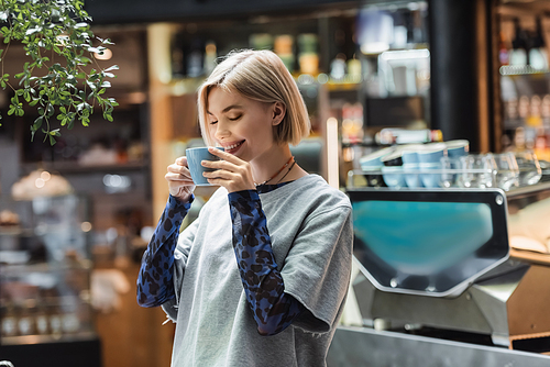 Positive woman with closed eyes holding cup in cafe