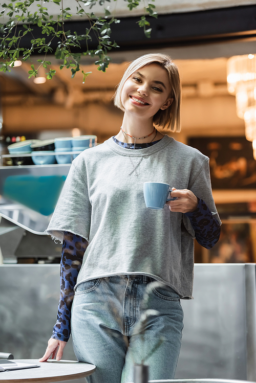 Positive woman holding cup and  in cafe