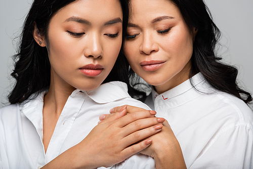 asian brunette mother and young daughter hugging each other and holding hands isolated on grey