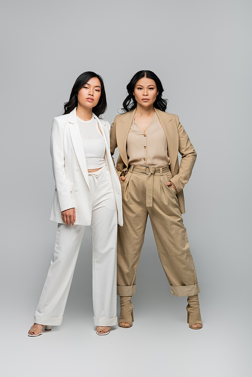 full length of stylish asian mother and daughter in suits posing on grey