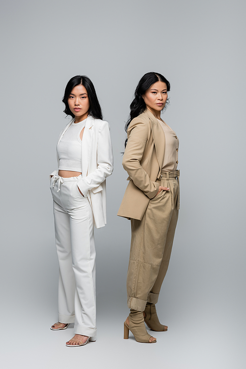 full length of stylish asian mother and young adult daughter in suits posing on grey