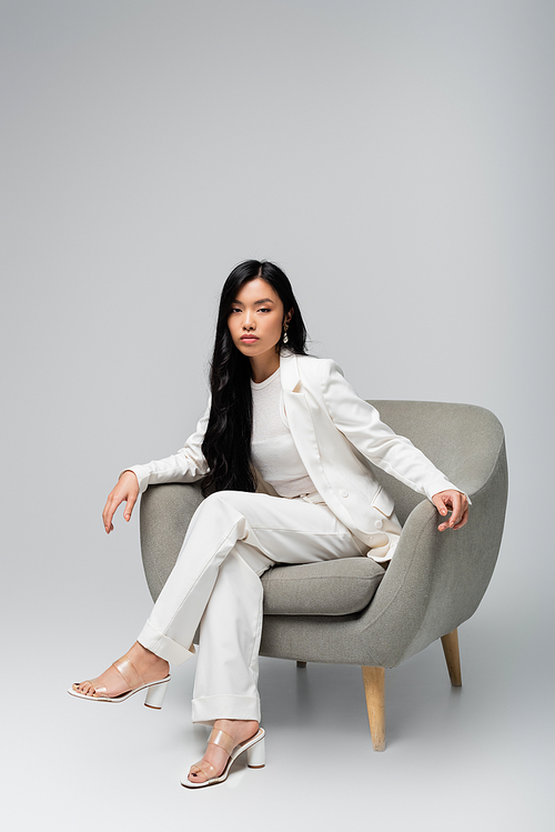 full length of young asian woman sitting in armchair on grey