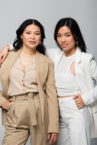 cheerful asian mother and daughter embracing isolated on grey