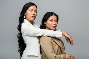 young asian woman hugging brunette mother in beige suit isolated on gray