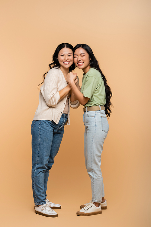 full length of happy asian mother and daughter holding hands on beige