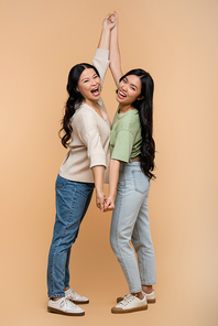 full length of amazed asian mother and daughter holding hands on beige