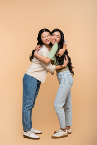 full length of cheerful asian mother and daughter hugging on beige