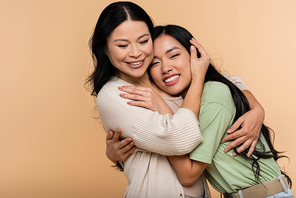 cheerful asian mother and daughter hugging isolated on beige