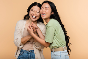cheerful asian mother and daughter holding hands isolated on beige