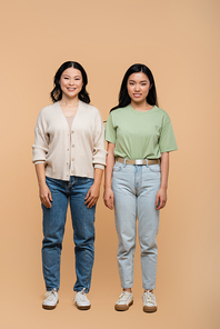 full length of cheerful asian mother and adult daughter standing on beige