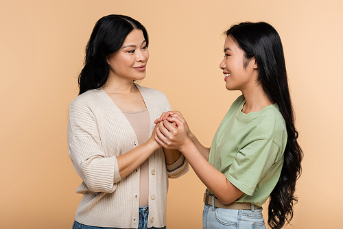 happy asian woman holding hands with adult daughter isolated on beige