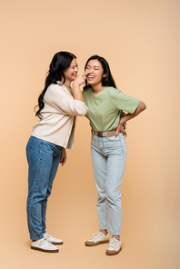 full length of cheerful asian mother touching nose of pleased young adult daughter on beige