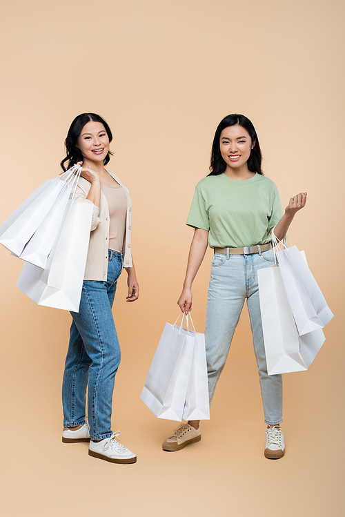 full length of happy asian mother and daughter with shopping bags on beige