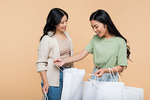 happy asian woman looking at shopping bag near mother isolated on beige