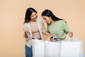 surprised asian woman looking at shopping bag near mother isolated on beige