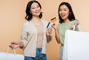cheerful asian mother and daughter with shopping bags and credit cards isolated on beige