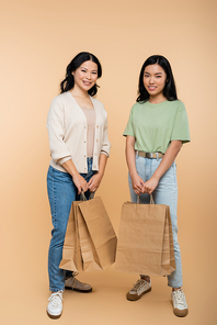 full length of happy asian mother and daughter with paper bags on beige