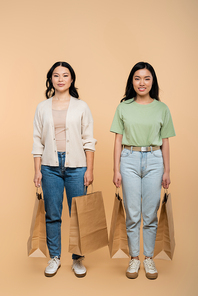full length of positive asian mother and daughter with paper bags on beige