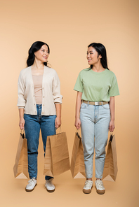 full length of cheerful asian mother and daughter with paper bags on beige
