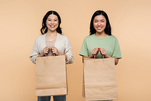happy asian mother and daughter with paper bags isolated on beige