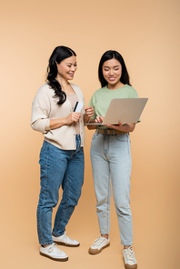 happy asian mother and adult daughter with credit card looking at laptop during online shopping on beige