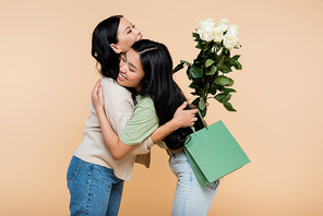 happy asian daughter congratulating and hugging mother isolated on beige