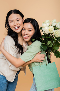 happy asian mother holding flowers and hugging adult daughter isolated on beige