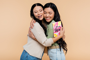 asian mother holding greeting card and hugging happy adult daughter isolated on beige