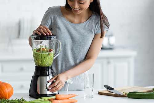 happy asian woman preparing vegetable smoothie for breakfast in kitchen