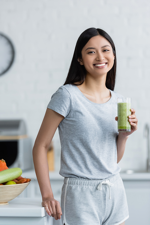 cheerful asian woman with glass of fresh smoothie  in kitchen