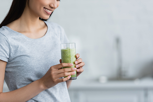 partial view of smiling woman holding glass of fresh homemade smoothie