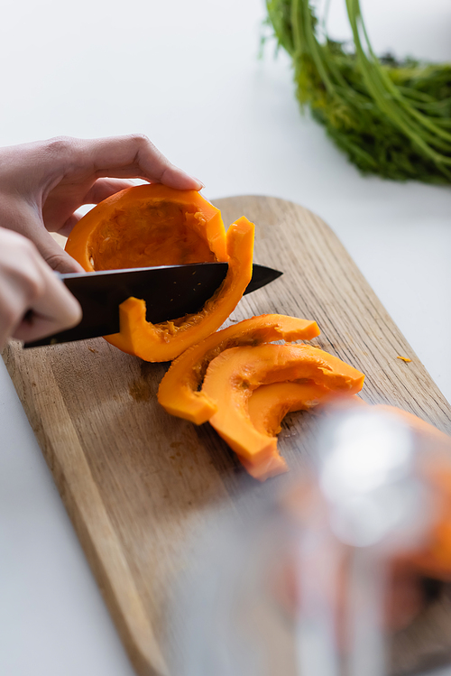 partial view of woman cutting ripe pumpkin on chopping board in kitchen
