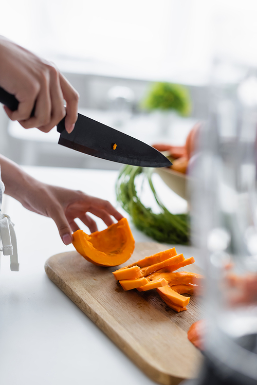 partial view of woman with knife near ripe pumpkin on cutting board, blurred foreground