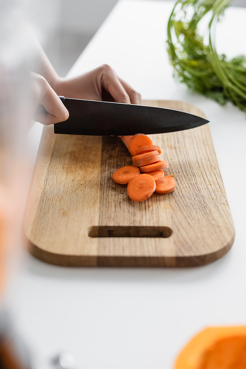 cropped view of woman cutting fresh carrot on chopping board, blurred foreground