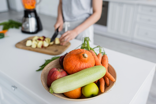 selective focus of bowl with fresh vegetables near blurred woman preparing breakfast in kitchen