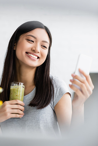 joyful asian woman with glass of fresh smoothie taking selfie on mobile phone