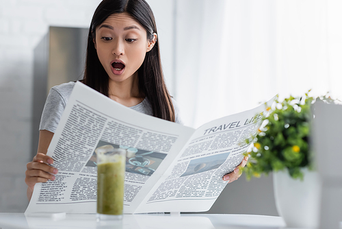 astonished asian woman reading travel life newspaper near blurred glass with smoothie
