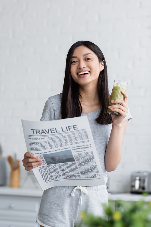 happy asian woman with travel life newspaper and glass of fresh smoothie  in kitchen
