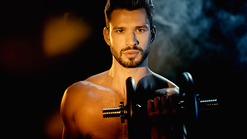 shirtless and muscular sportsman training with dumbbell near smoke on black