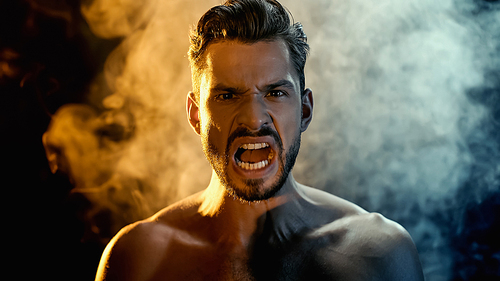 Portrait of irritated sportsman screaming and  with smoke on black